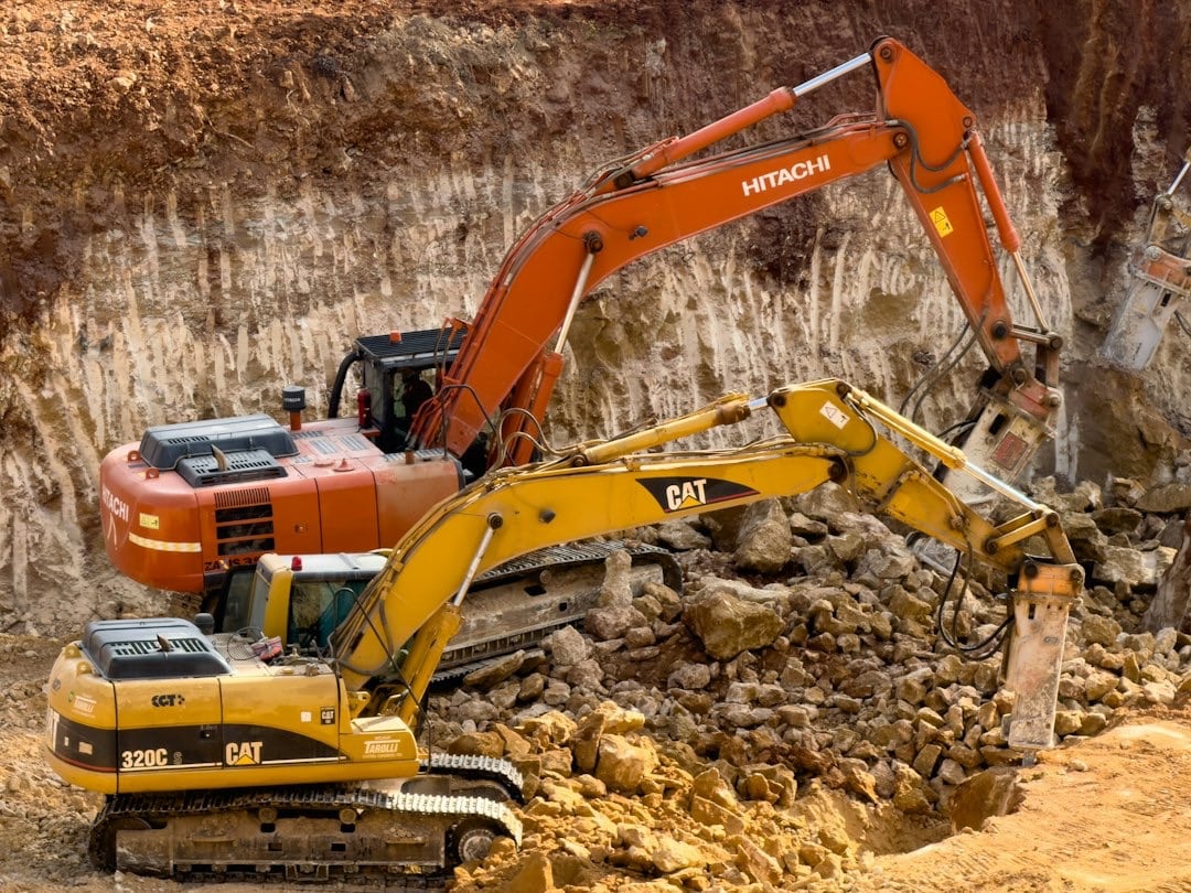 Orange and yellow excavators break rock in a deep pit.