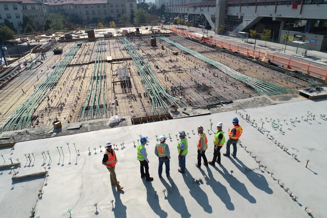 Construction workers in safety vests observe a building site.